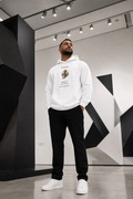 A man wearing a white "Founder Mindset" graphic hoodie, black pants, and white sneakers standing in a modern studio with geometric black-and-white background architecture.