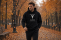Man walking through an autumn park wearing a black Mindful Craftsman "OPERATE IN SILENCE" hoodie with falling golden leaves.